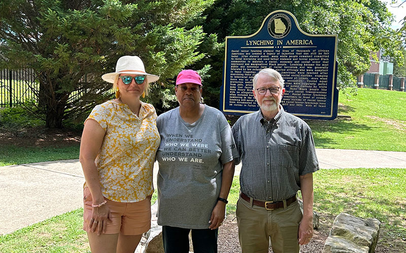 Three members of the coalition standing in a park in front of a monument remembering lynchings in America